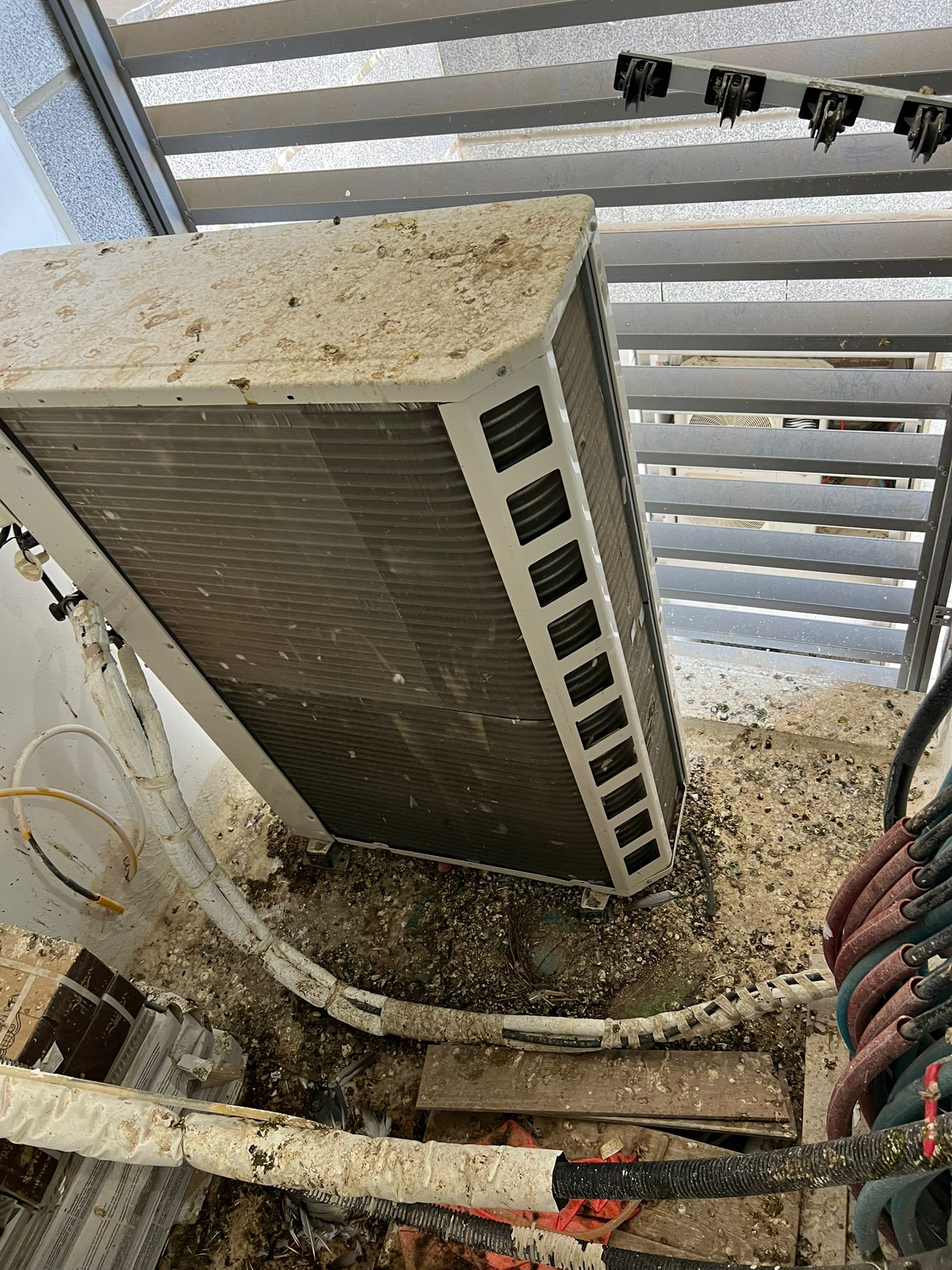 יחידת מזגן חיצונית מכוסה בצואת יונים ובשאריות קן לפני ניקוי