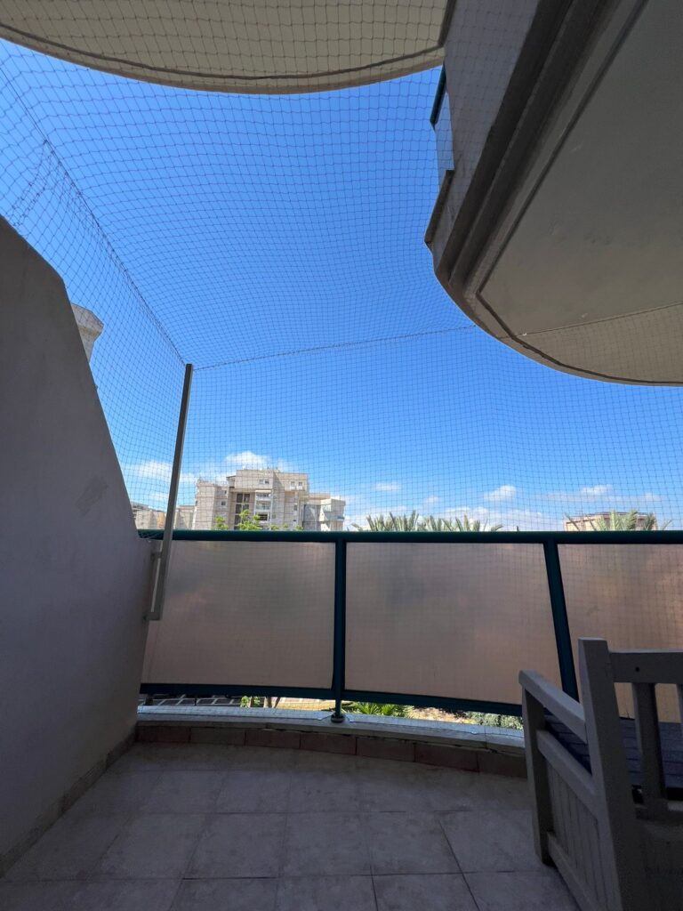רשת נגד יונים מותקנת במרפסת שמש מול שמיים כחולים