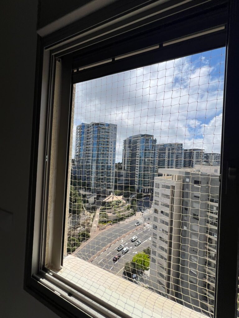 רשת נגד יונים מותקנת על חלון דירה במגדל מגורים עם נוף לבניינים